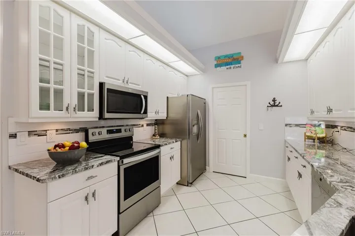 Kitchen with stainless steel appliances, tasteful backsplash, glass insert cabinets, and light stone countertops