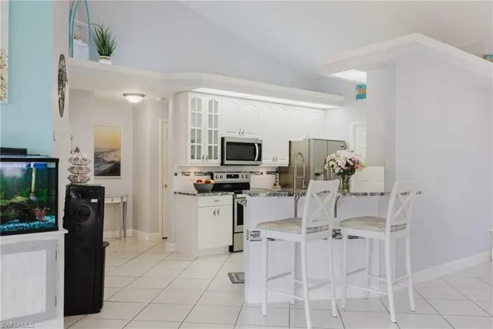 Kitchen with stainless steel appliances, a breakfast bar, glass insert cabinets, white cabinets, and light tile patterned floors