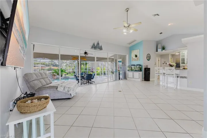 Living area with ceiling fan, lofted ceiling, light tile patterned floors, and a sunroom