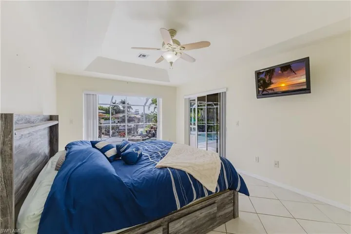 Bedroom with access to exterior, light tile patterned flooring, baseboards, a ceiling fan, and a tray ceiling
