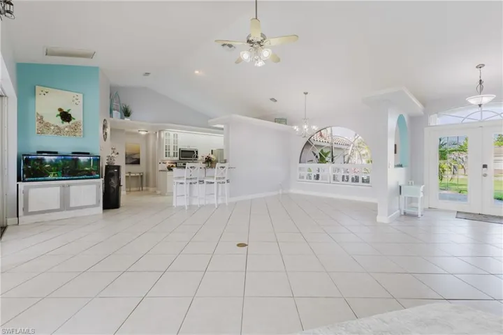 Unfurnished living room with plenty of natural light, light tile patterned flooring, ceiling fan, a chandelier, and high vaulted ceiling