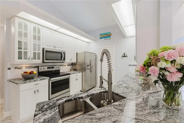 Kitchen with stainless steel appliances, a sink, light stone counters, glass insert cabinets, and decorative backsplash