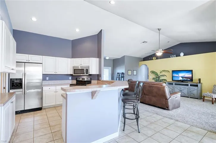 Kitchen featuring white cabinetry, stainless steel appliances, a kitchen breakfast bar, light colored carpet, and lofted ceiling