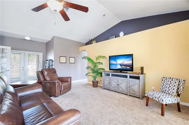 Living room with ceiling fan, light carpet, and vaulted ceiling