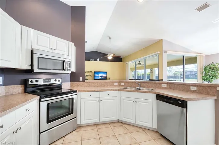 Kitchen featuring ceiling fan, white cabinets, stainless steel appliances, and vaulted ceiling
