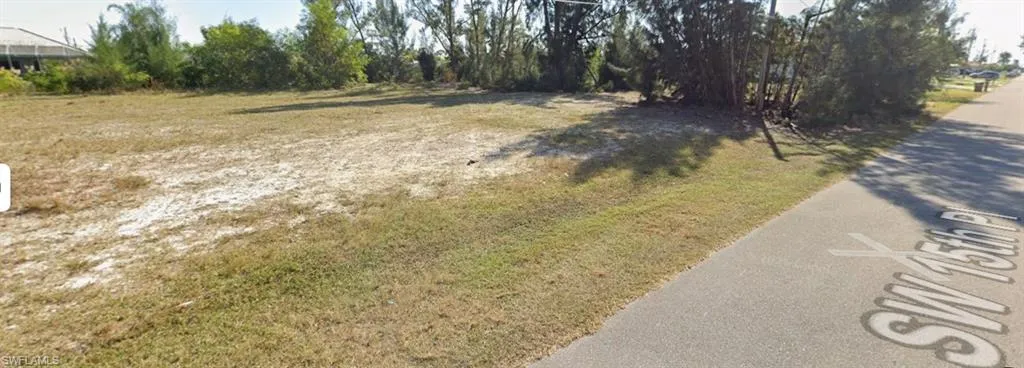 Spacious lot featuring a paved road frontage with street name inscription, partial grass cover, and mature perimeter trees