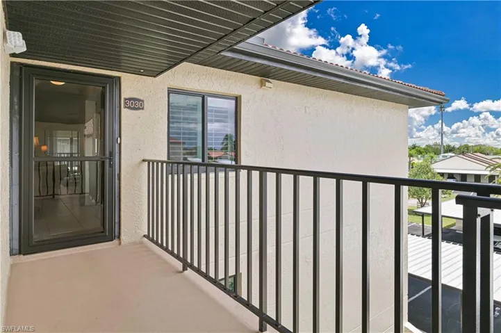Exterior balcony featuring a full-light storm door, adjacent window with blinds, and a black wrought iron railing