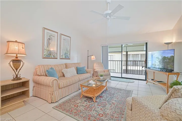Spacious living area featuring neutral tile flooring, a ceiling fan, and a floor-to-ceiling sliding glass door leading to a screened balcony with black railings