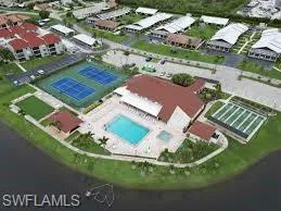 Community hub featuring a swimming pool, spa, two tennis courts, and a shuffleboard court, bordered by a dark-hued body of water and lush green landscaping