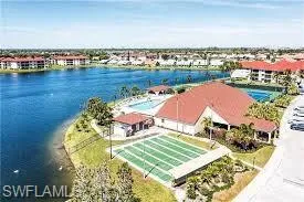 Resort-style recreational area featuring a large swimming pool, tennis courts, and a multi-purpose sports court, all set against a prominent waterfront