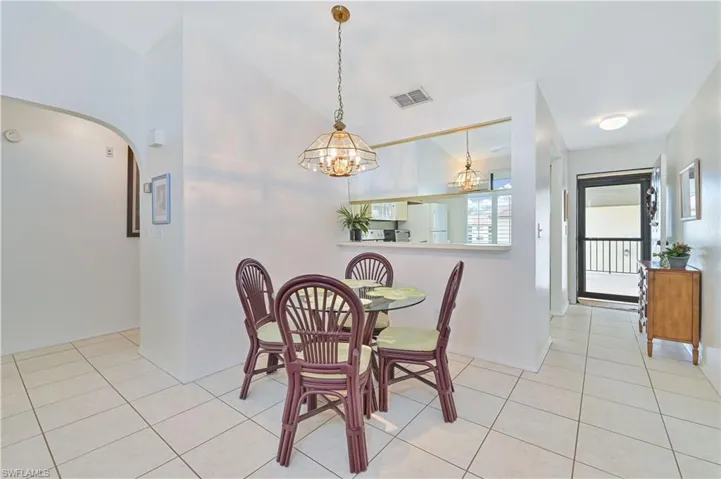 Open-concept dining area featuring a decorative chandelier, white tile flooring, and a pass-through opening to the kitchen