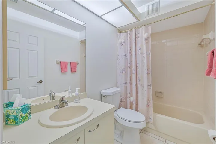 Bathroom featuring a single vanity with an integrated sink, a large mirror, and a tub/shower combination with tiled walls
