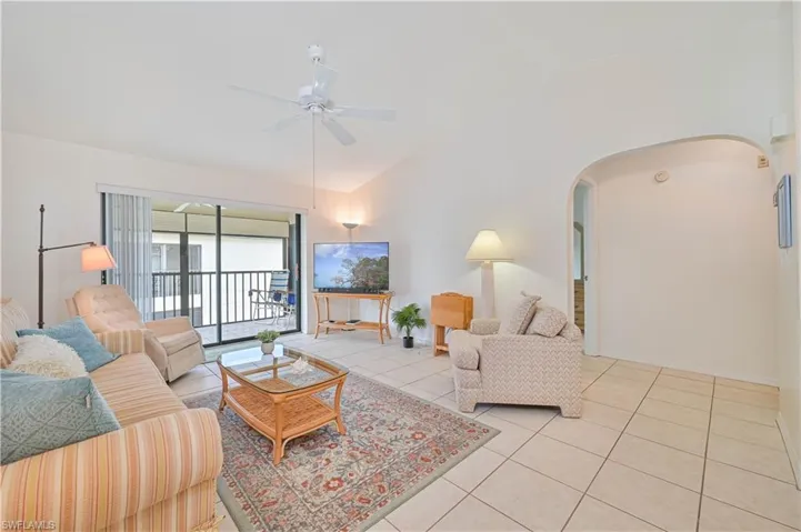 Living area featuring large format tile flooring, a vaulted ceiling, a ceiling fan, and an arched entry