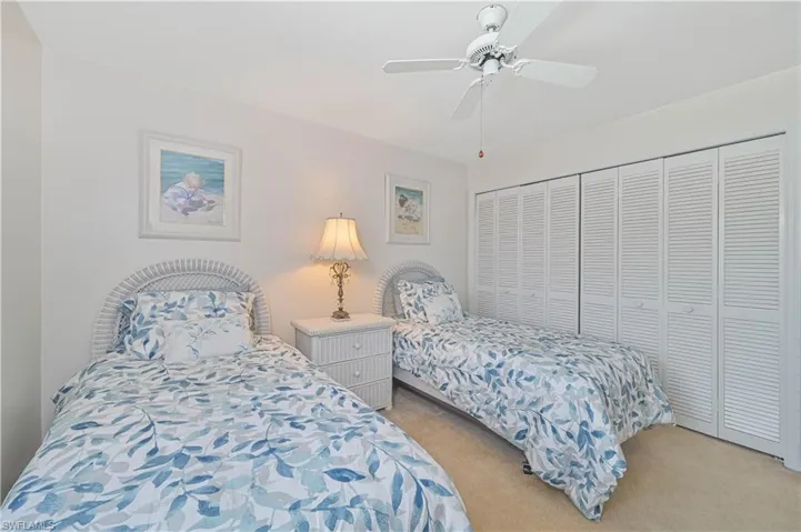 Room featuring two beds with wicker headboards, a ceiling fan, and louvered bifold closet doors