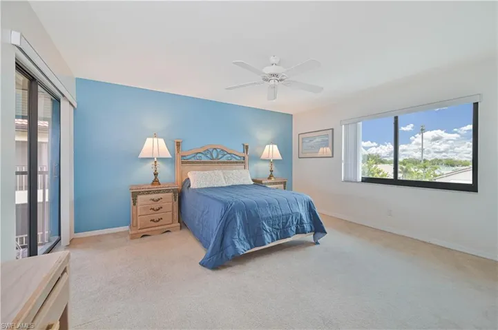 Carpeted room featuring a light blue accent wall, a ceiling fan, and a large window with a horizontal blind