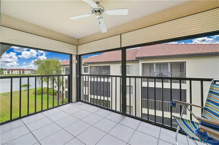 Screened balcony featuring white square tile flooring, black metal railings, a ceiling fan, and a serene water backdrop