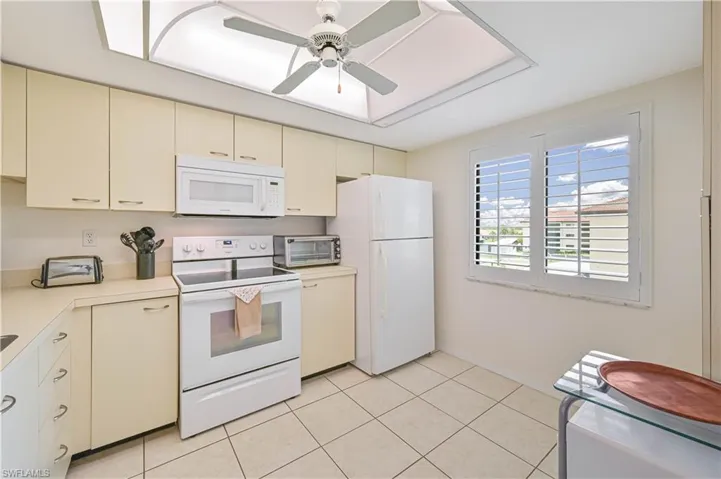 Kitchen featuring cream-colored cabinetry, white appliances, and a tiled floor