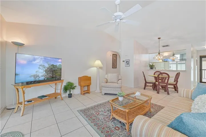 Open concept living space featuring vaulted ceilings, tile flooring, a ceiling fan, and a pass-through breakfast bar with pendant lighting