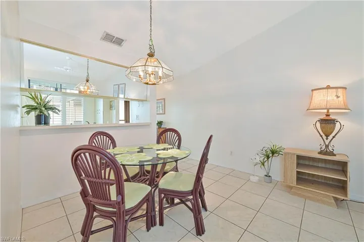 Dining area featuring tile flooring, a decorative ceiling light fixture, a pass-through window with mirror accents, and white painted walls