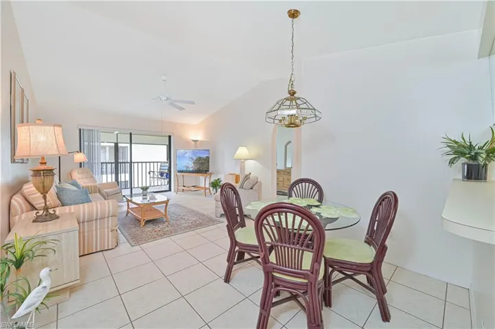 Open-concept living and dining area featuring tile flooring, vaulted ceilings, and a sliding glass door leading to a private balcony