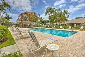 Outdoor swimming pool featuring a paver deck, surrounding lounge chairs, a cabana structure, mature palm trees, and established landscaping