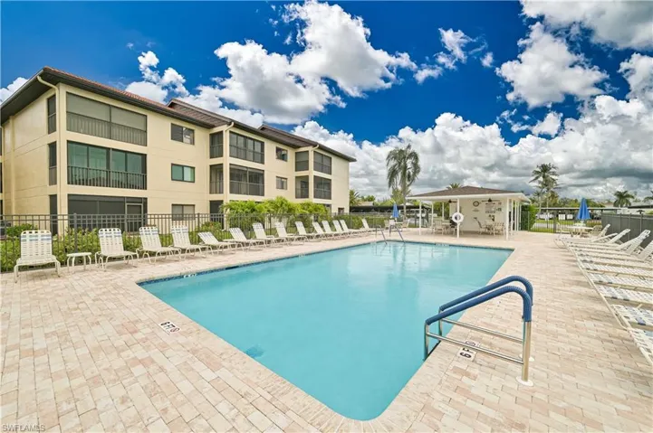 Outdoor swimming pool with a paved deck, surrounded by lounge chairs and a covered pavilion