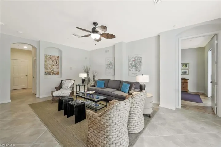 Living room with light tile patterned floors, baseboards, visible vents, arched walkways, and ceiling fan