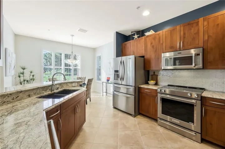 Kitchen with light tile patterned floors, backsplash, a sink, light stone counters, and appliances with stainless steel finishes