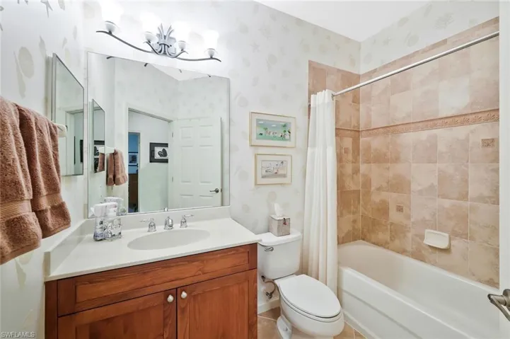 Full bathroom toilet, vanity, shower / bathtub combination with curtain, and wallpapered walls