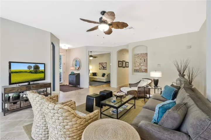 Living room with light tile patterned floors, visible vents, arched walkways, and ceiling fan