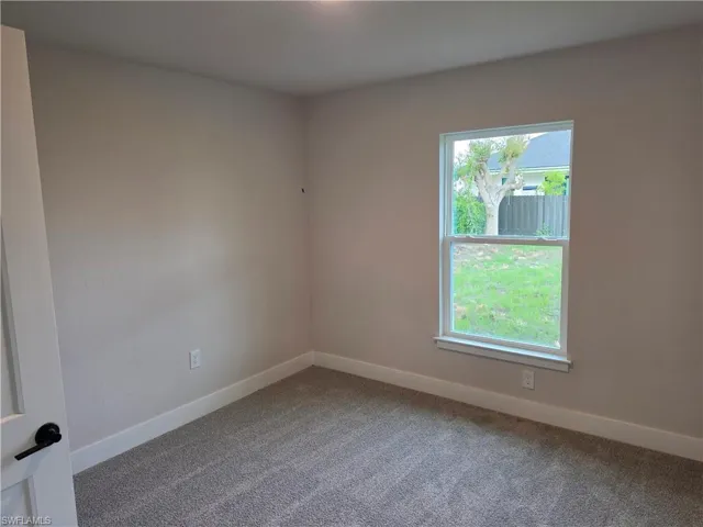 Light-filled room featuring neutral wall tones, plush gray carpeting, white trim, a double-hung window, and a modern interior door with matte black hardware