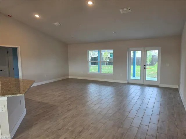 Spacious living area featuring plank-style tile flooring, vaulted ceilings with recessed lighting, and a kitchen island with a stone countertop