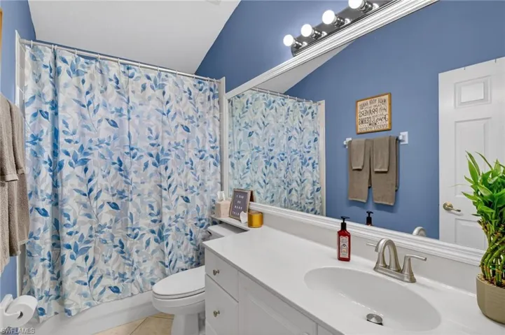 Bathroom with vanity, shower / bath combo with shower curtain, light tile patterned flooring, and vaulted ceiling