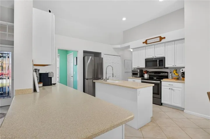 Kitchen with stainless steel appliances, white cabinetry, a center island with sink, light tile patterned floors, and a high ceiling