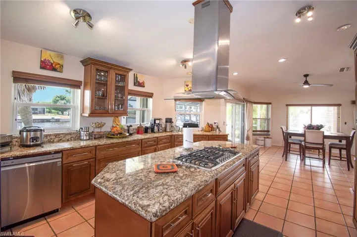 Kitchen with stainless steel appliances, island exhaust hood, light tile patterned flooring, brown cabinets, and ceiling fan