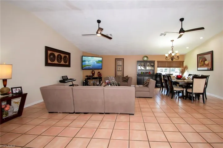 Living area with lofted ceiling, light tile patterned flooring, and ceiling fan with notable chandelier