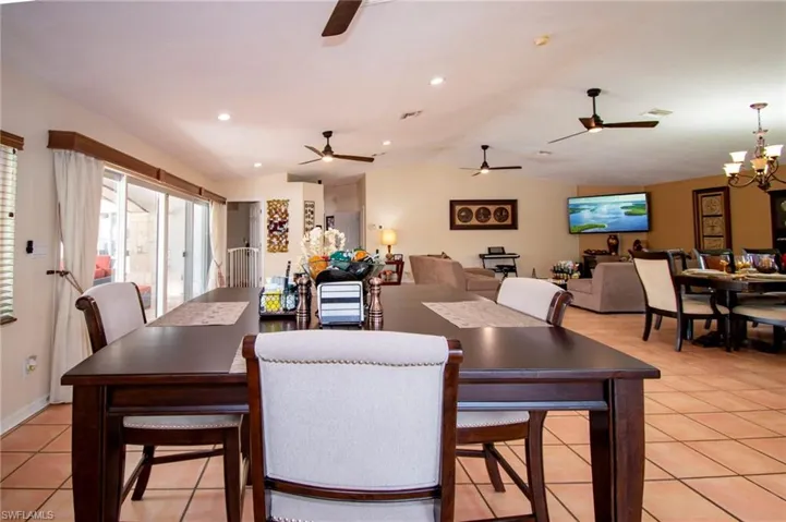 Dining area with light tile patterned floors, vaulted ceiling, visible vents, and ceiling fan with notable chandelier