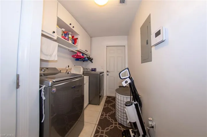 Washroom featuring electric panel, washer and clothes dryer, light tile patterned flooring, visible vents, and cabinet space
