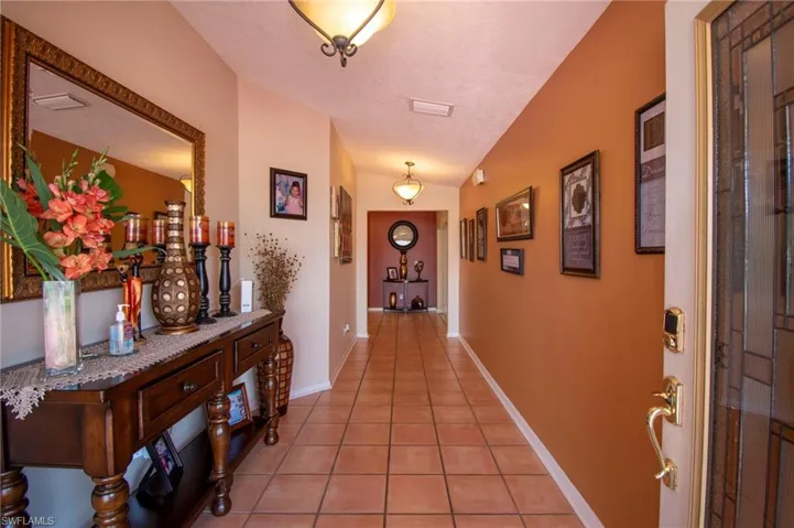 Hall featuring baseboards, vaulted ceiling, and light tile patterned floors