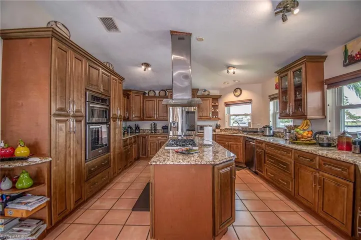 Kitchen featuring open shelves, visible vents, island range hood, light tile patterned floors, and appliances with stainless steel finishes