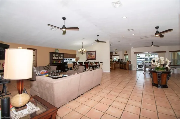 Living room with light tile patterned flooring, vaulted ceiling, visible vents, and ceiling fan with notable chandelier