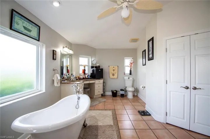 Full bath featuring a ceiling fan, tile patterned floors, vanity, a soaking tub, and toilet