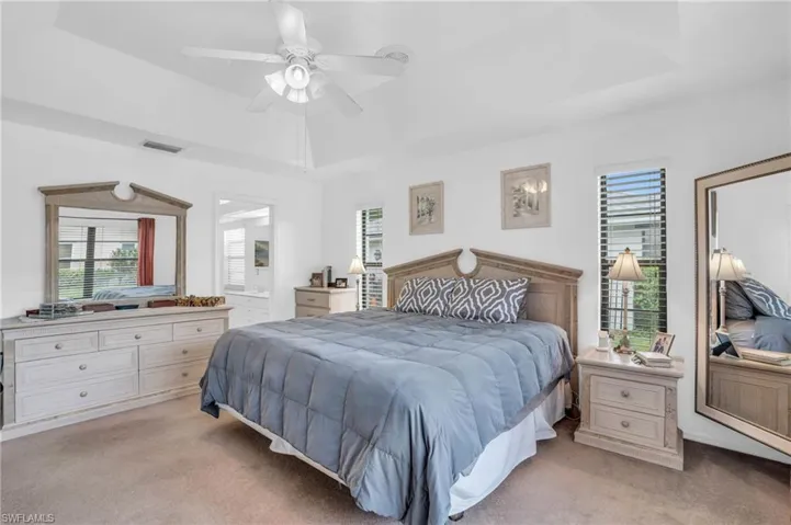 Bedroom featuring a raised ceiling, light colored carpet, and ceiling fan