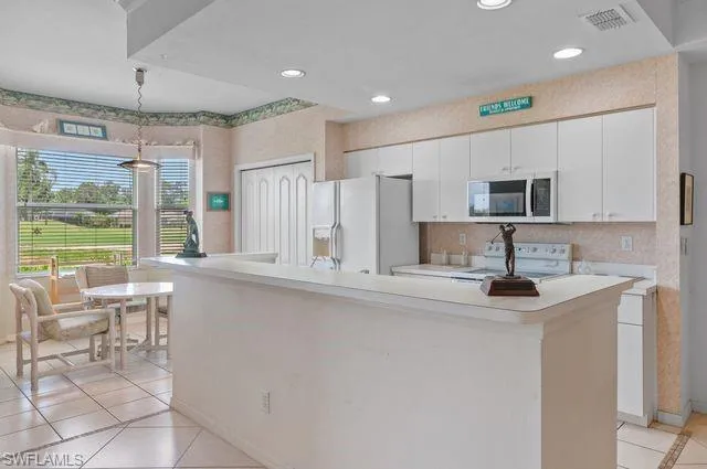 Kitchen featuring light tile patterned floors, light countertops, white appliances, white cabinetry, and decorative light fixtures