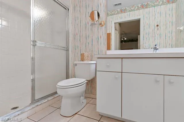 Bathroom featuring wallpapered walls, a stall shower, vanity, and tile patterned flooring