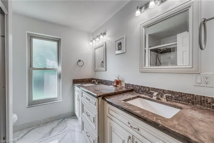 Bathroom with two vanities, a sink, baseboards, a shower with door, and marble finish floor