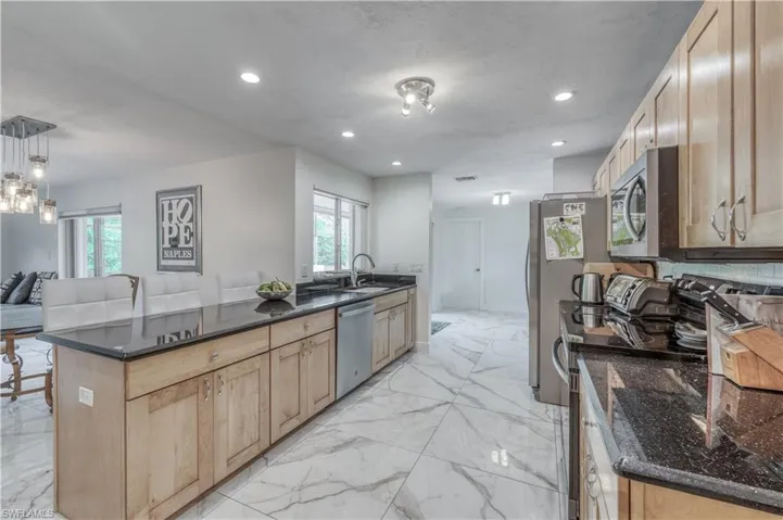 Kitchen featuring dark stone counters, light brown cabinetry, marble finish floor, stainless steel appliances, and recessed lighting