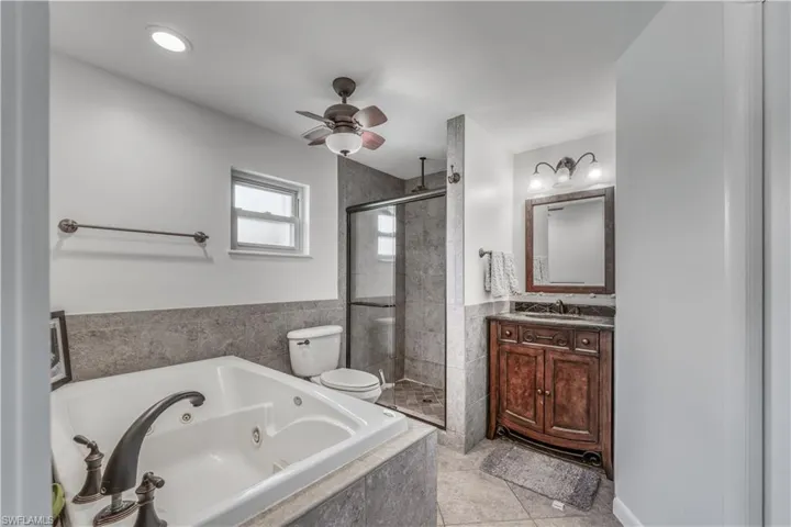 Full bathroom featuring ceiling fan, a tub with jets, vanity, and a stall shower