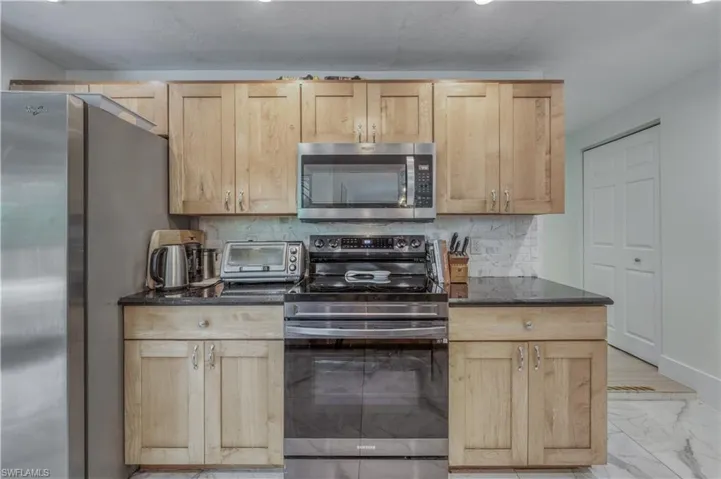 Kitchen with marble finish floor, light brown cabinetry, a toaster, stainless steel appliances, and backsplash