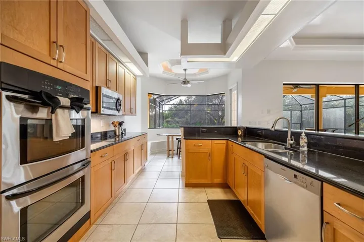 Kitchen featuring stainless steel appliances, quartz countertops, a tray ceiling, and bay windows with built-in bench for table.